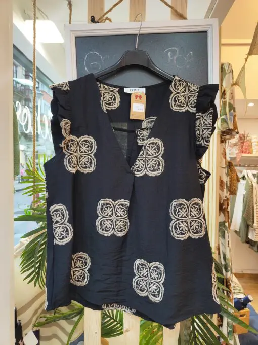Blusa escote pico con pinza central, volante en la sisa. Tiene corte evase que le da amplitud en la cadera. El pantalon cintura de goma con dos pinzas en la parte delantera y corte de pierna ancho. Las dos prendas levan bordados en color beige.