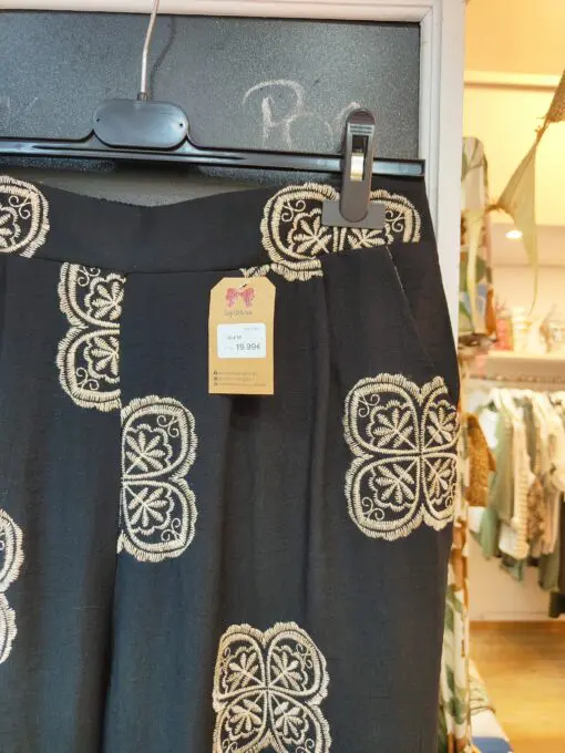 Blusa escote pico con pinza central, volante en la sisa. Tiene corte evase que le da amplitud en la cadera. El pantalon cintura de goma con dos pinzas en la parte delantera y corte de pierna ancho. Las dos prendas levan bordados en color beige.