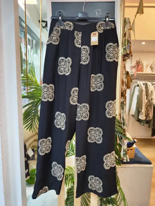 Blusa escote pico con pinza central, volante en la sisa. Tiene corte evase que le da amplitud en la cadera. El pantalon cintura de goma con dos pinzas en la parte delantera y corte de pierna ancho. Las dos prendas levan bordados en color beige.