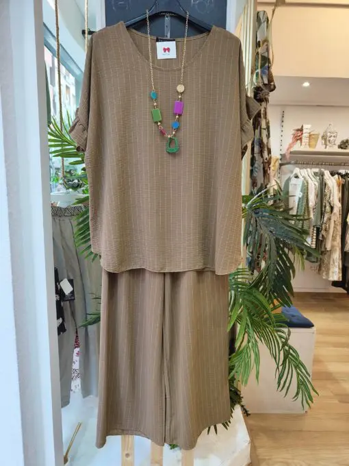 Conjunto dos piezas raya diplomatica compuesto por bluson de corte cuadrado con volante en la sisa y pantalon de goma elástica y pata ancha tipo palazzo. Para completar el look incluye un precioso colgante .
