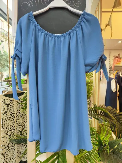 Blusa fluida azul. Blusa fluida con escote elástico tipo barco, ideal para llevar con los hombros al aire. Detalle de lazo en las mangas cortas que le aporta un toque femenino y elegante. Su tejido suave y ligero la convierte en una prenda perfecta para el verano.